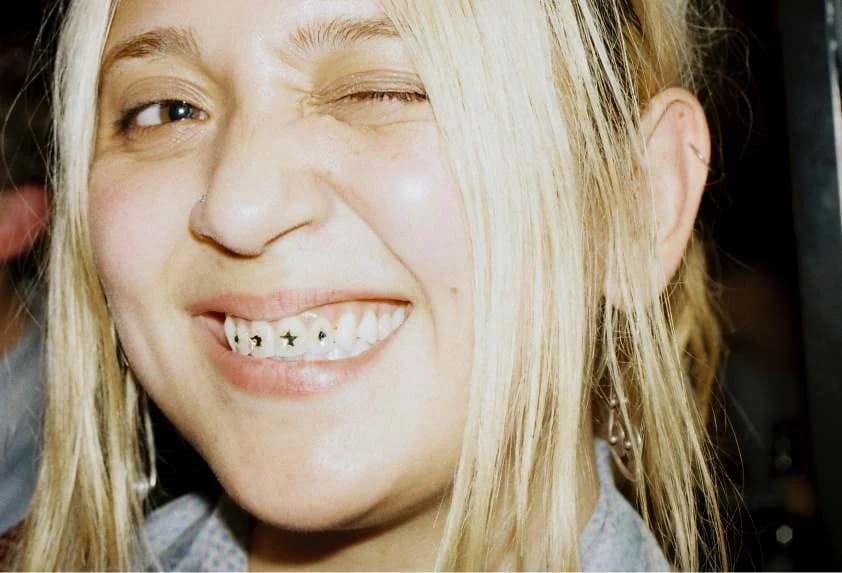 A guest at Designers’ Night in Paris winks and smiles at the camera, showing small stars set on their teeth.